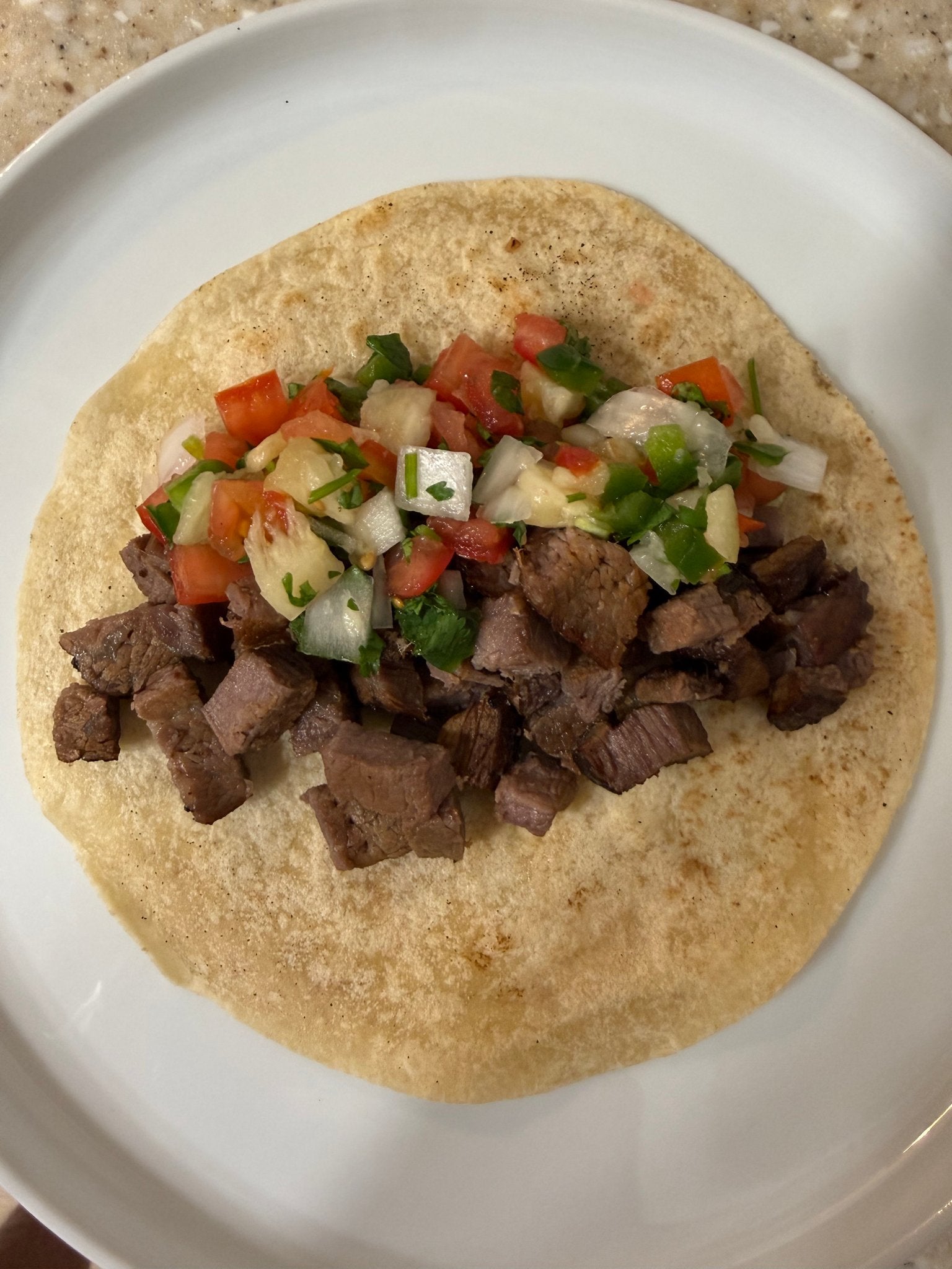 Grilled beef taco topped with Hawaiian pineapple pico de gallo on a corn tortilla