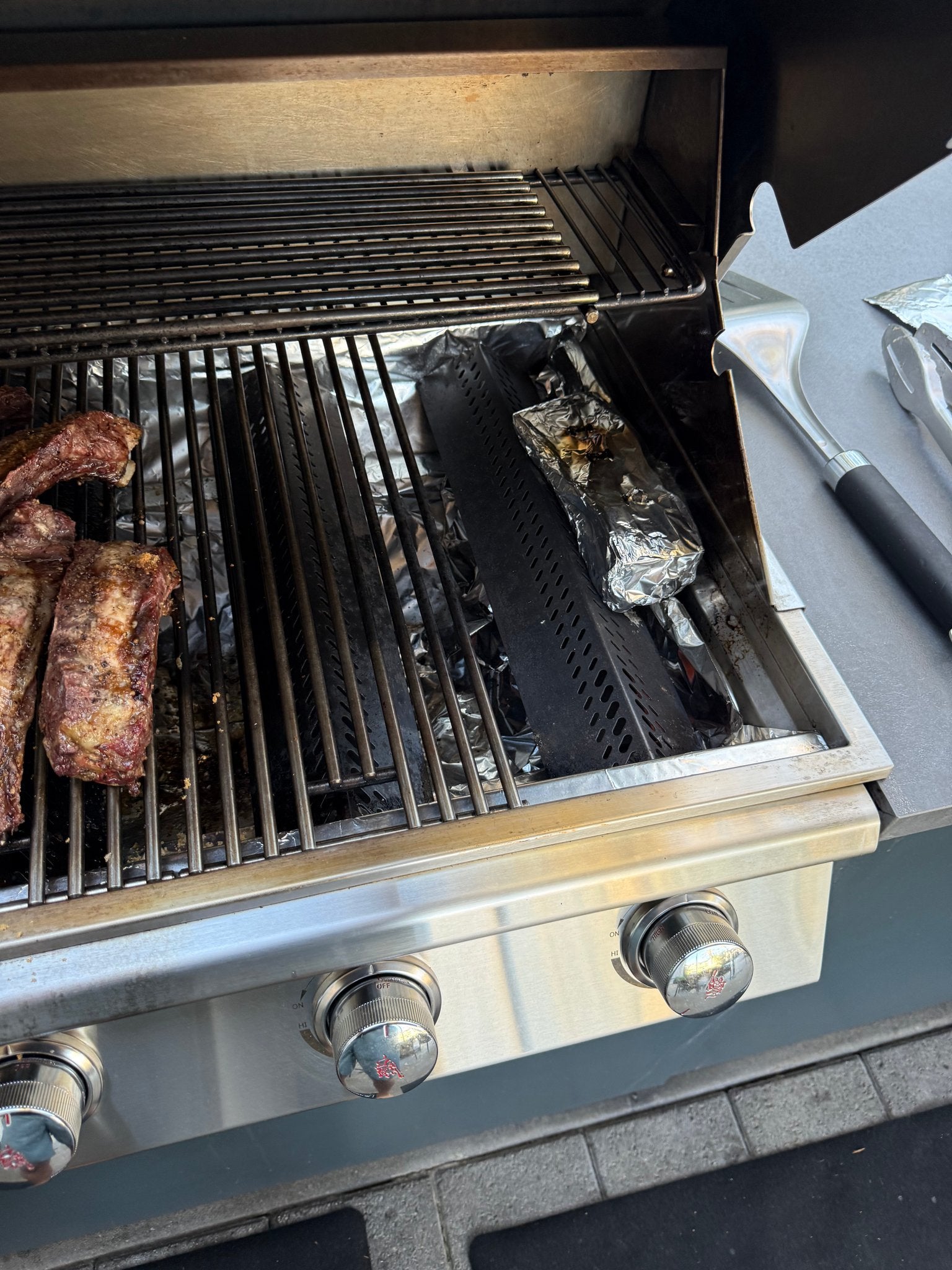 Foil pouch of kiawe wood chips over the lit burner, turning a gas grill into a Hawaiian smoker